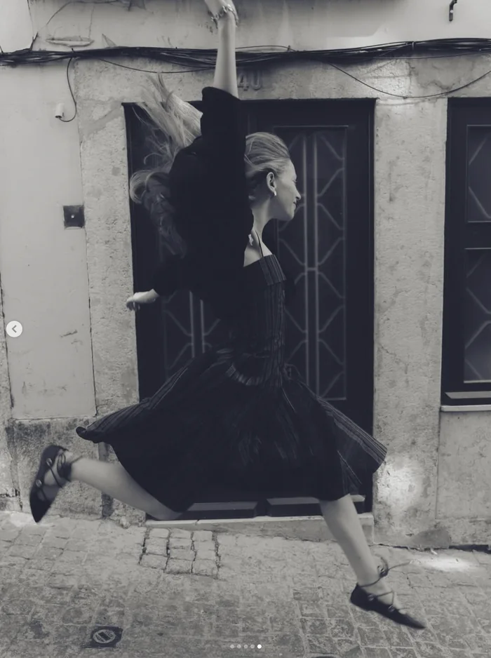 Black and white photo of a woman in a black dress jumping in a Lisbon street