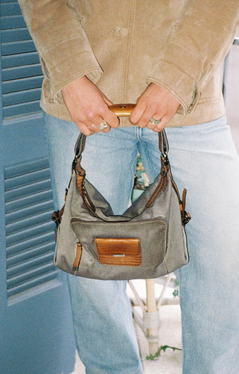 Khaki bag with leather handle held in front of light jeans