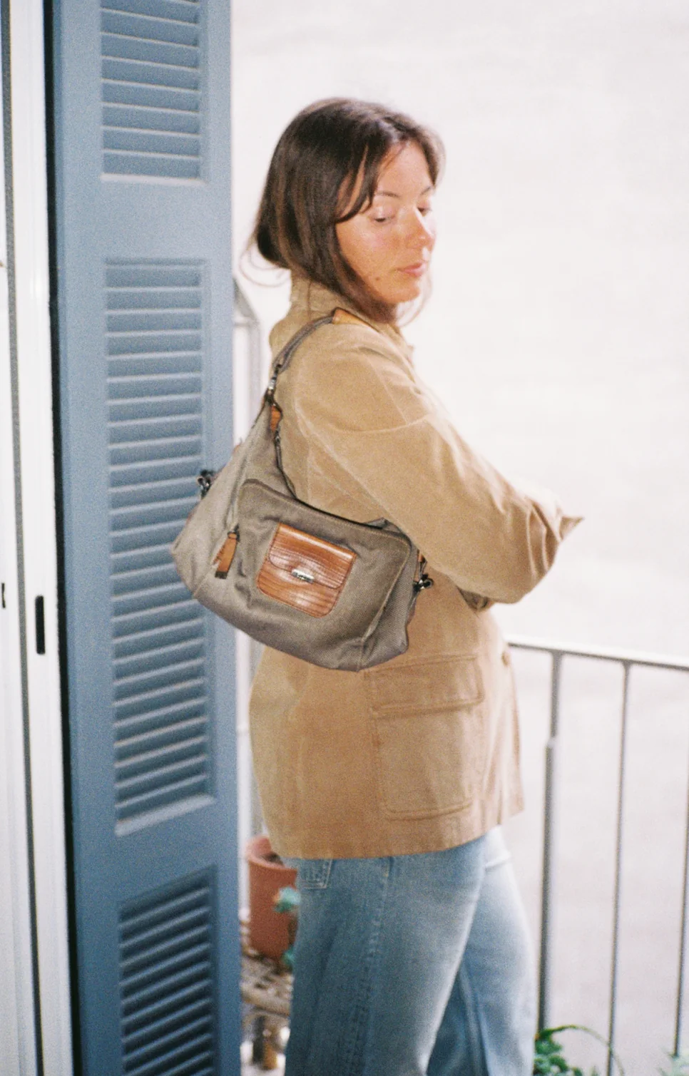 Khaki bag worn on the shoulder with a suede jacket by a blue shutter