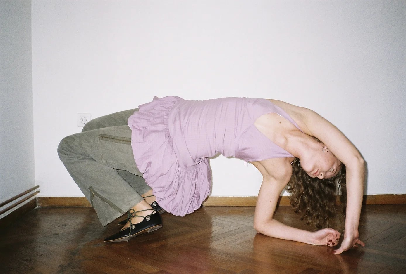 Woman in a lilac ruffled top bending backwards on a wooden floor