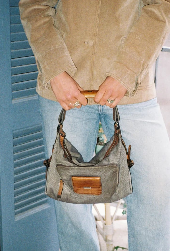 Khaki bag with a leather handle held in front of light jeans