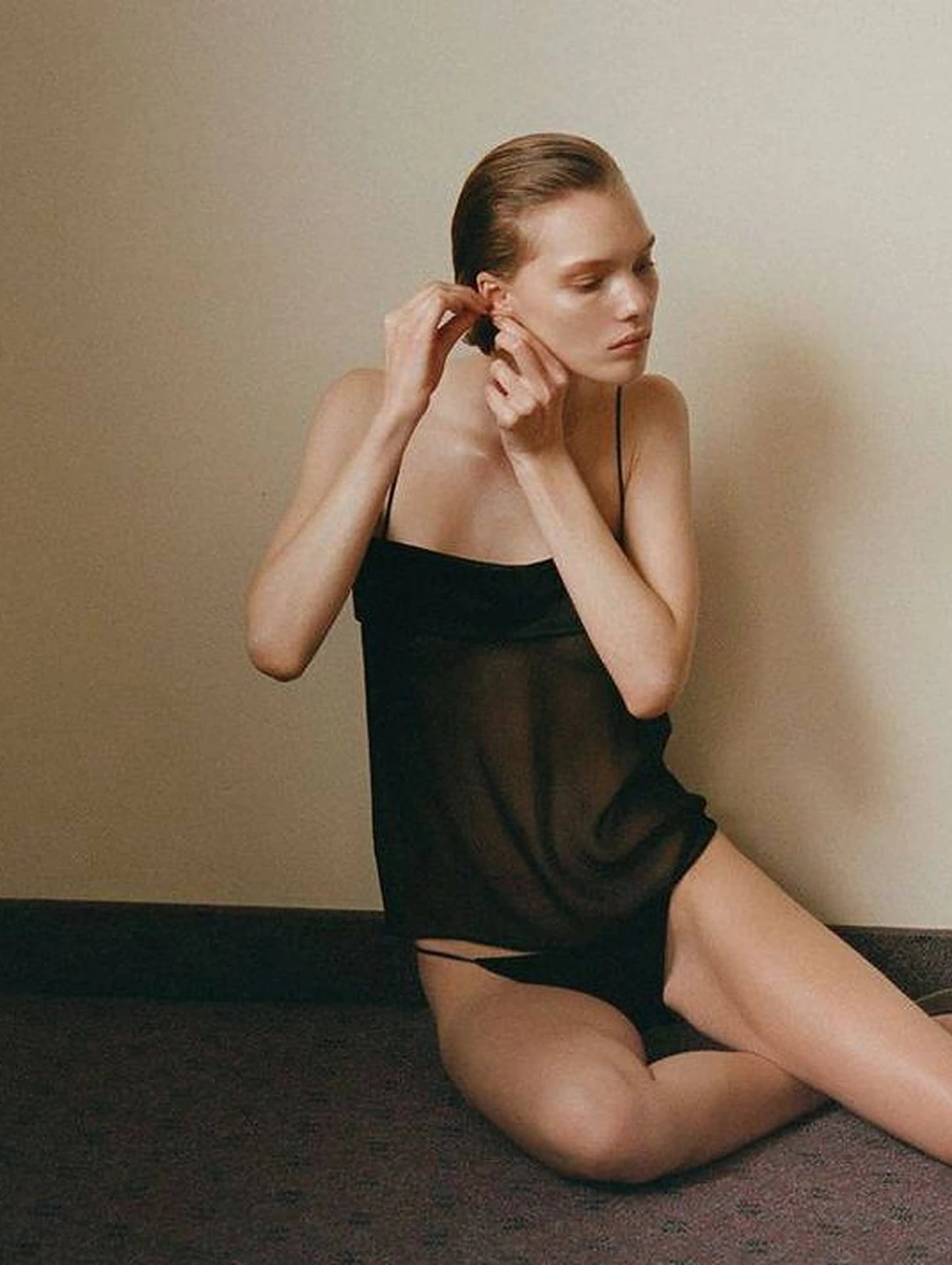 Woman in a sheer black slip sitting on a carpeted floor