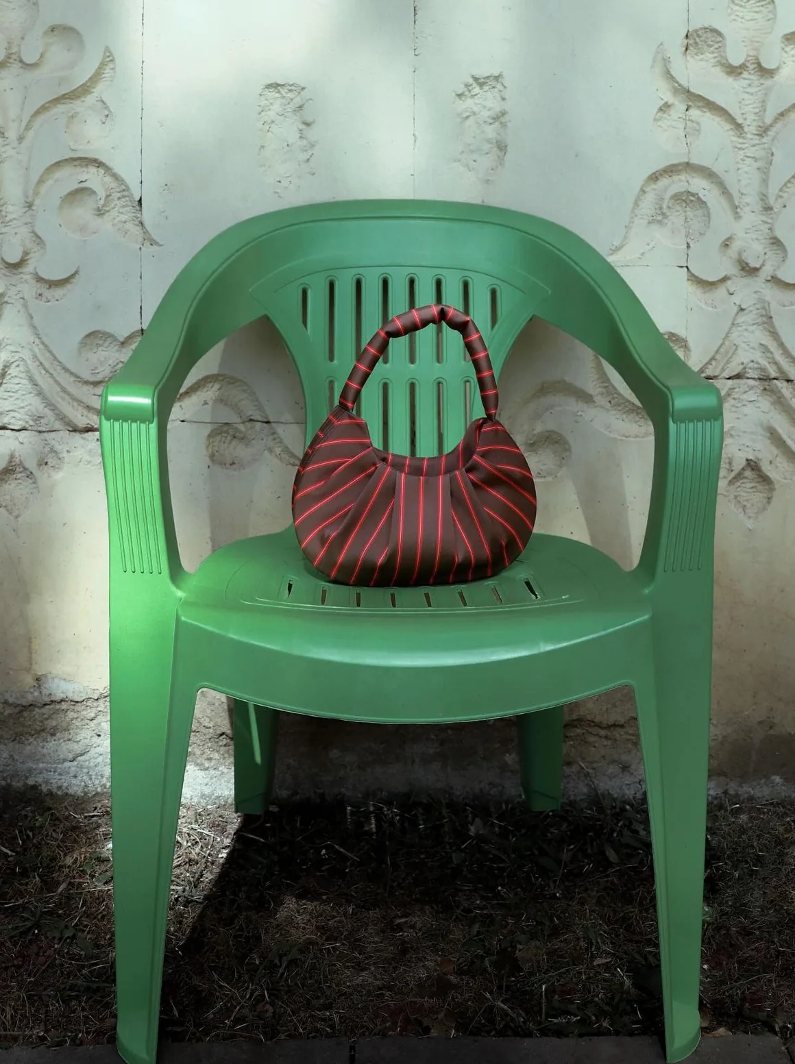 Red striped bag on a green plastic chair against an ornate wall