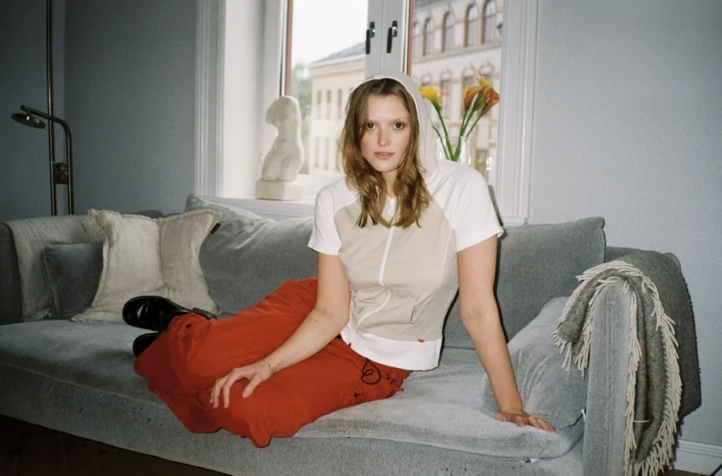 Woman on a grey sofa in a white zip top and red trousers